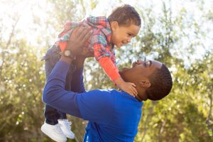 A man in a bright blue shirt holding a boy in the air