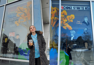 Young women holding a coffee standing in front of a mural